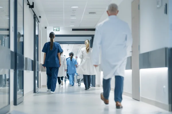 Corredor do hospital com médicos, enfermeiros e especialistas. Médicos, cirurgiões e profissionais de saúde caminham juntos no corredor, de costas para a câmera. SUS