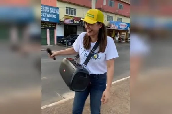 Imagem colorida de mulher com boné amarelo e caixa de som pendurada