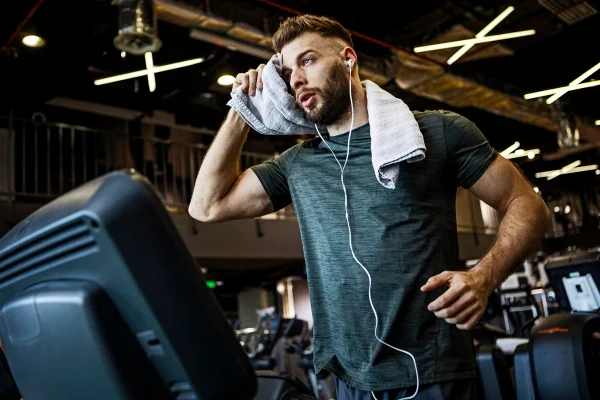 Jovem atleta correndo em uma esteira em uma academia enquanto ouve música. Metrópoles