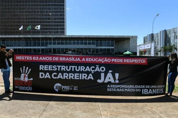 Fotografia colorida de duas pessoas estendendo faixa preta com palavras em branco