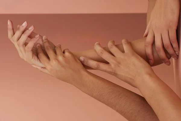 Mãos de três pessoas juntas em fundo rosa - Metrópoles