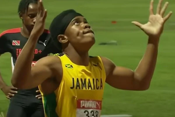 Atleta veste camisa amarela da Jamaixa e tem as duas mãos e a cabeça levantadas para cima