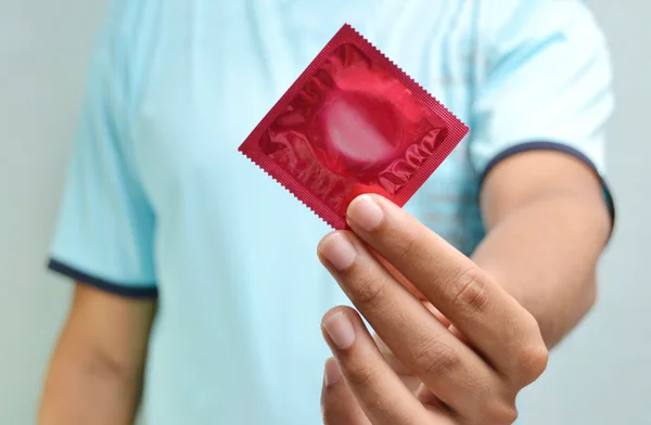 Foto mostra homem segurando embalagem de camisinha de tom vermelho