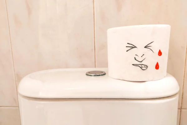 Foto colorida de vaso sanitário feito de cerâmica, com um rolo de papel higiênico e um desenho de um rosto fazendo força - Metrópoles.