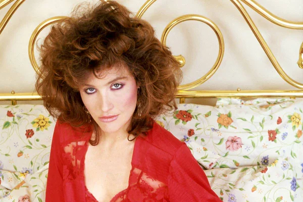 Foto colorida de Robyn Bernard usando roupa vermelha e sentada em cama - Metrópoles