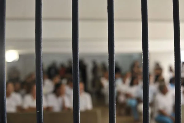 Imagem desfocada de mulheres atrás das grades de um presídio