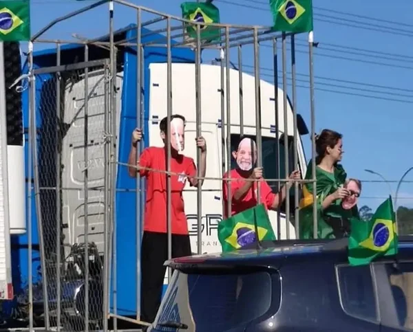 Foto mostra crianças com máscaras do presidente eleito Lula e do ministro do STF, Alexandre de Moraes, presas em jaulas sob caminhão em manifestação bolsonarista, na cidade de Balenário Camboriu (SC). Várias bandeiras do Brasil adornam o local - Metrópoles
