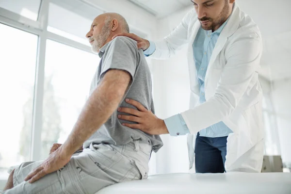 Foto colorida de fisioterapeuta fazendo massagem em coluna de homem que está sentado - Metrópoles