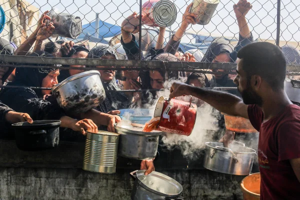 Palestinos recebem refeições quentes distribuídas por organizações humanitárias na área de al-Mawasi, em Khan Yunis, Gaza