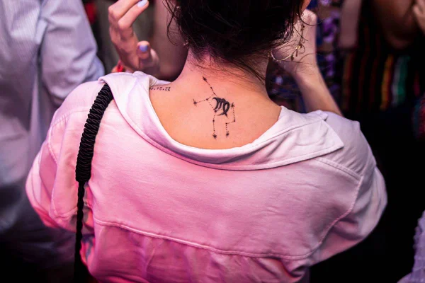 mulher de costas com camisa rosa e tatuagem do signo de