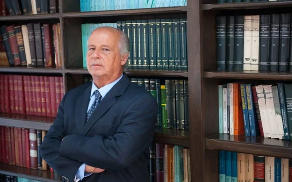 Imagem colorida de um homem de terno e gravata em frente a livros - Metrópoles