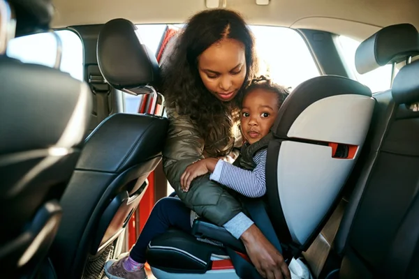 Mãe e filha dentro do carro enquanto a mulher prende a criança na cadeirinha