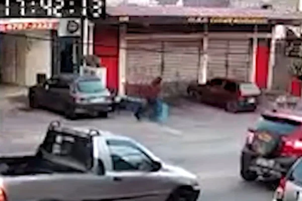 Imagem colorida de homem com blusa avermelhada com capuz correndo por calçada de avenida - Metrópoles