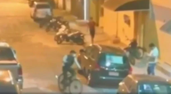 imagem colorida mostra frame de cena gravada por câmera de segurança em que aparecem um ciclista armado e um homem vestido de branco mexendo no celular - metrópoles
