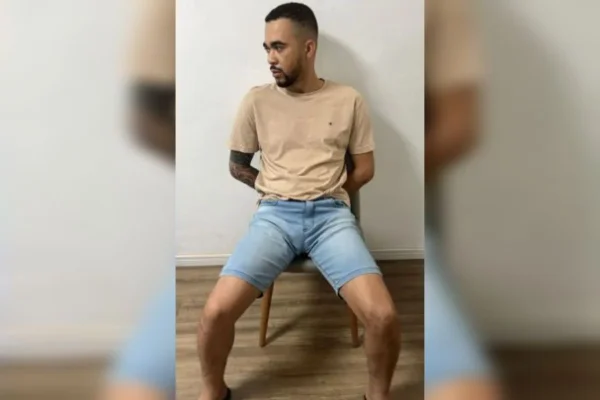 Homem sentado, com o rosto virado para a direita, vestindo camiseta marrom e shorts jeans - Metrópoles