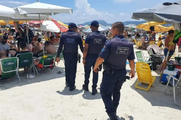 Imagem colorida mostra policiais fazendo fiscalização do uso de caixas de som em praia do litoral de São Paulo - Metrópoles