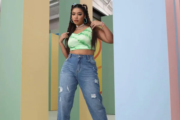 Mulher negra com cabelo longo liso. Ela usa um top verde, uma calça jeans. As peças são da marca Shein.