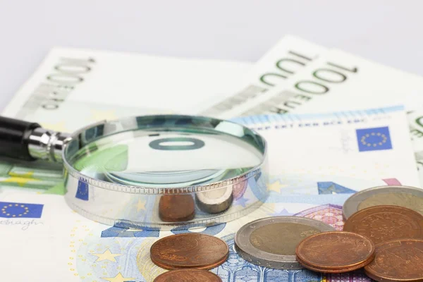 Imagem colorida de uma lupa sobre notas e moedas de euro - Metrópoles
