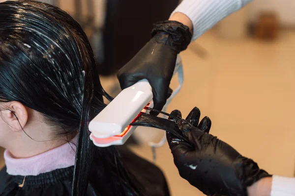 Imagem mostra uma mulher passando chapinha no cabelo molhado, como em um alisamento - Metrópoles