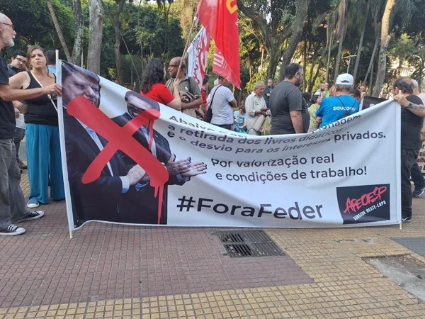 Imagem colorida mostra professores segurando uma faixa branca com as fotos do governador Tarcísio de Freitas e do secretário de Educação, Renato Feder, com um X vermelho em cima deles. No texto da faixa, está a inscrição #foraFeder - Metrópoles