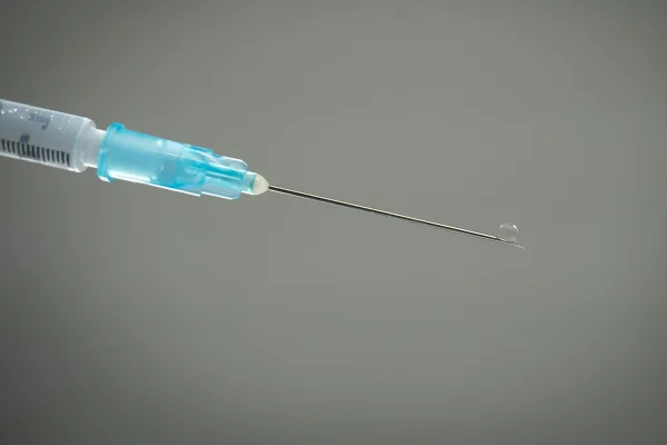 Foto colorida de seringa com fluído saindo em agulha com fundo cinza - Metrópoles.