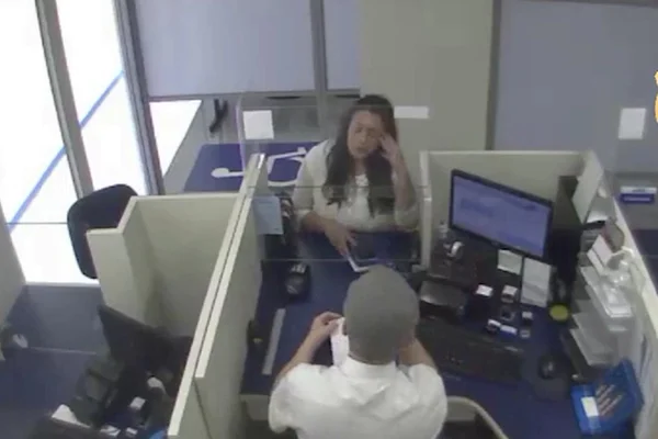 mulher de cabelo preto e longo sentada em frente a funcionário de banco