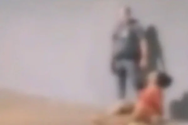 Imagem colorida de policial atrás de mulher algemada sentada na calçada. Metrópoles