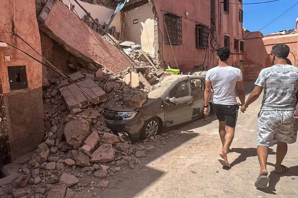 Foto colorida de dois homens e um carro soterrado após terromoto no Marrocos