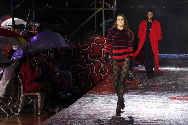 Julia Fox na passarela da Tommy Hilfiger, usando meia-calça de renda com logomania e body com estética de suéter estampado com listras azuis e vermelhas
