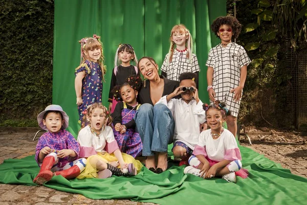A apresentadora Sabrina Sato sentada com várias crianças ao seu redor. A foto é da campanha publicitária da marca Sato Kid