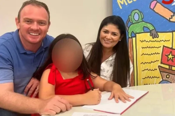 Imagem colorida de um homem e uma mulher, segurando uma criança com o rosto borrado