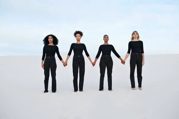 Foto colorida - Quatro mulheres vestidas de preto de mãos dadas