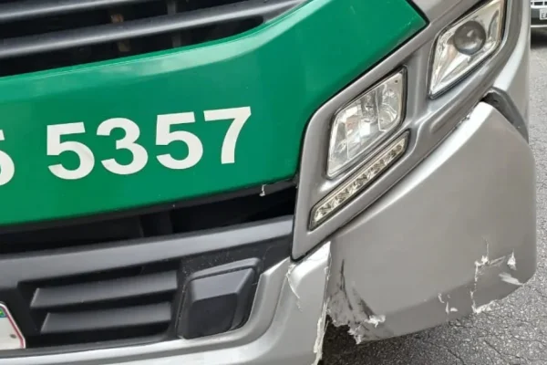 Imagem colorida mostra frente de ônibus danificada do lado esquerdo, no para-choque