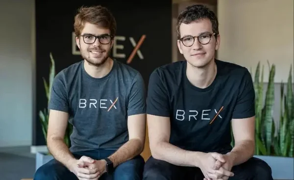 Foto colorida de dois homens sentados. Eles estão com uma blusa, com a palavra Brex. Os dois usam óculos - Metrópoles