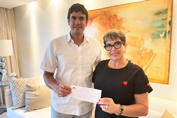 Homem de branco e mulher de preto segurando papel e sorrindo para foto
