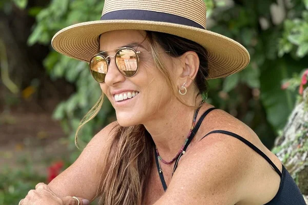 Monique Curi posa, sorridente, com óculos escuros e chapéu - Metrópoles