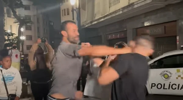 Manifestante, homem branco de camiseta cinza e barba dá soco com o braço direito no rosto do ex-deputado Arthur do Val, homem branco de camisa preta - Metrópoles