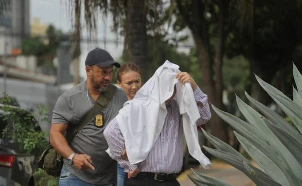 foto colorida de três pessoas em pé, uma dela está cobrindo a cabeça