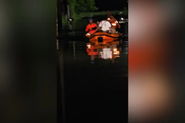 Imagens coloridas mostram frame de vídeo que mostram barco da Defesa Civil navegando em alagamento na cidade de Peruíbe