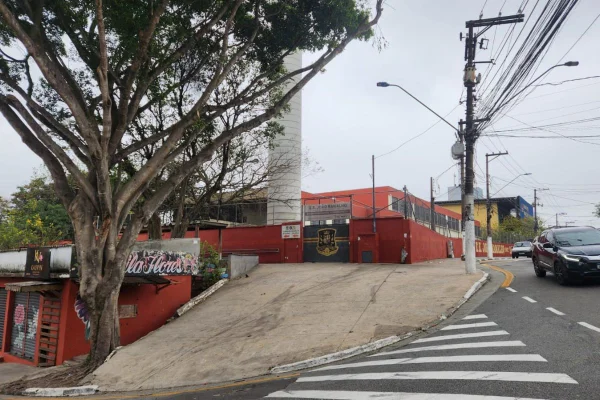 imagem colorida mostra fachada de escola em diadema. cena mostra portão da escola, árvore na esquina da rua, faixa de pedestes e parte da rua