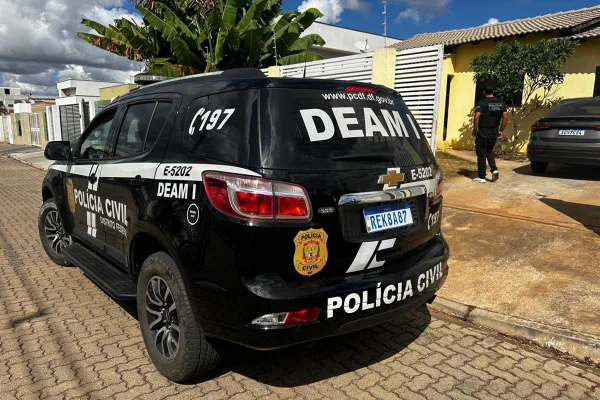 Foto colorida de carro com caracterização da delegacia da mulher do distrito federal em frente a casa