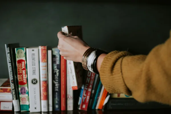Imagem colorida mostra pessoa pegando livros de uma estante - Metrópoles