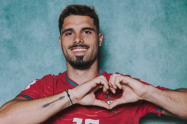 Foto colorida de homem fazendo coração com as mãos. Ele está com a blusa da Seleção de Portugal - Metrópoles