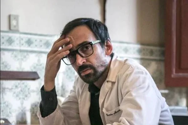 foto colorida de homem com a mão na cabeça usando óculos e jaleco branco