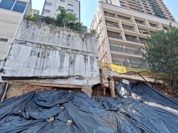 Imagem mostra monte de terra coberto por lona preta com alicerces à mostra ao fundo - Metrópoles