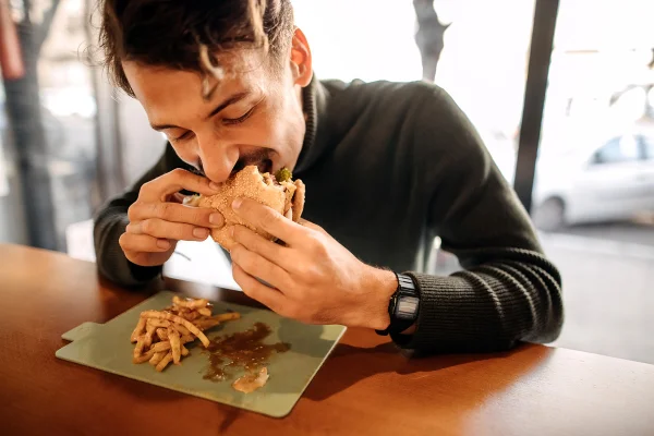Homem comendo lanche, hamburguer e batata frita. Metrópoles