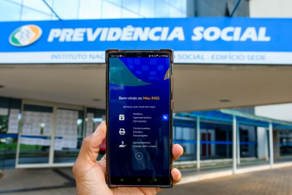 Fachada da Previdência Social e acesso digital aos serviços do INSS pelo aplicativo Meu INSS - Mertrópoles