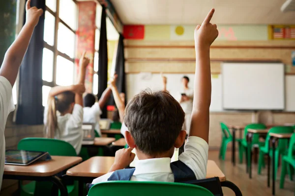 aluno, de costas, com a mão levantada em uma sala de aula crises climáticas