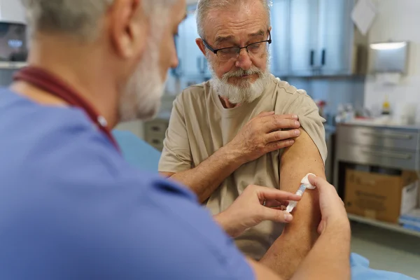 Imagem mostra idoso branco de barba sendo vacinado por homem de uniforme médico - Metrópoles