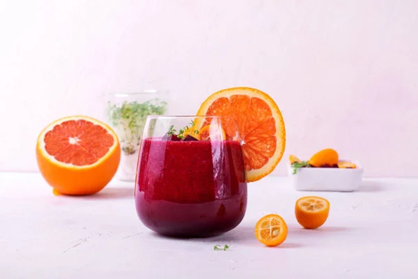 Imagem colorida de copo de suco de barraja e fatias de laranja do lado em fundo salmão - Metrópoles